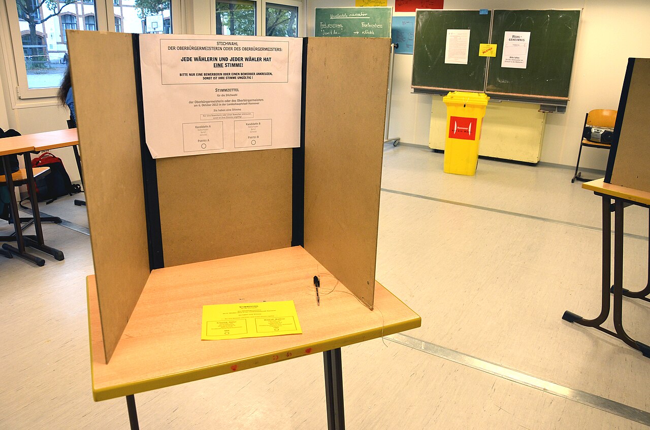 Wahlkabine mit Sichtschutz und Wahlurne im Hintergrund - Symbolbild für die Stimmabgabe bei einer deutschen Wahl.
